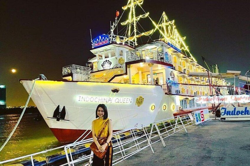 Un barco grande e iluminado llamado 'Indochina Queen' atracado en un puerto, con una persona de pie al frente. 2