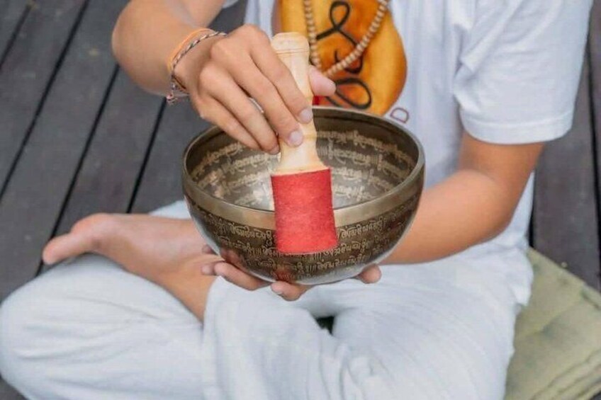 A person sitting cross-legged on a wooden deck, holding a singing bowl with a red cloth inside. 3