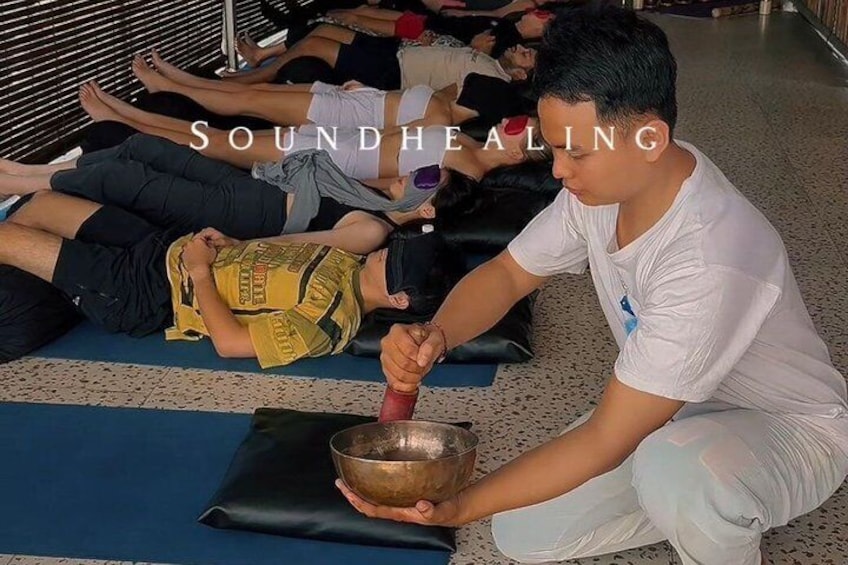 A group of people participating in a sound healing session, lying on mats with a practitioner using a bowl. 5