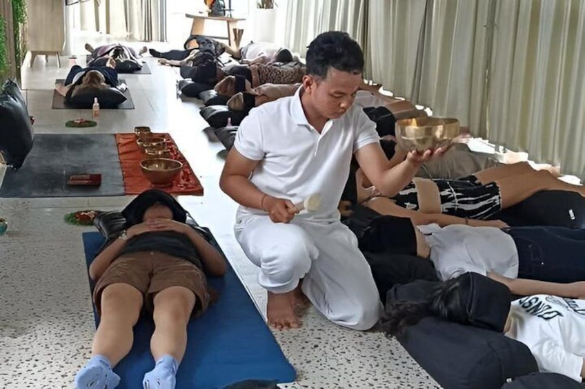 A group of people in a meditative pose, some lying on mats, others kneeling, with a person holding a bowl. 2
