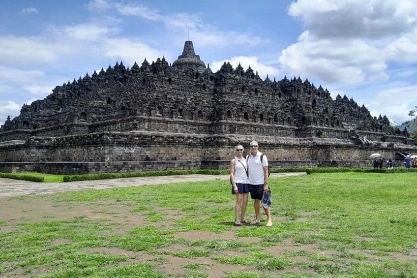 A large ancient temple complex with multiple tiers and a central spire, surrounded by a grassy area. 1