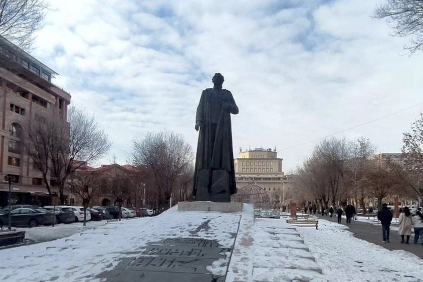 A statue on a pedestal, a snow-covered street, and buildings in the background. 1