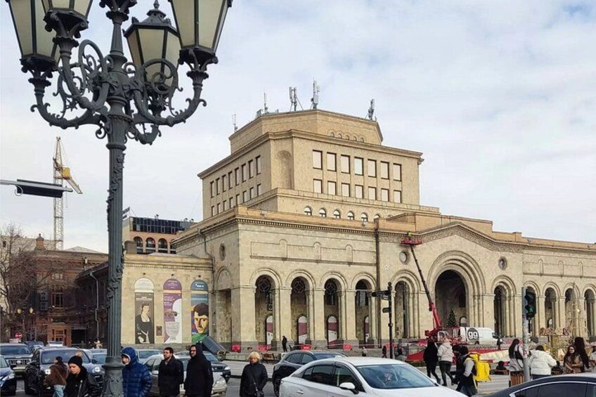 A historic building with arched windows and a central tower, surrounded by a busy street with pedestrians and cars. 3