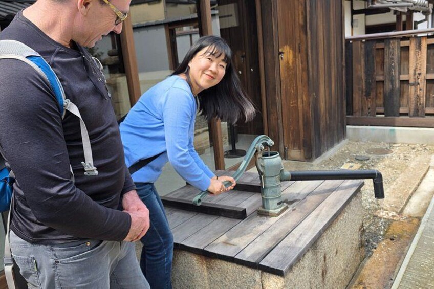 A man and a woman interacting with a water pump outdoors. 3