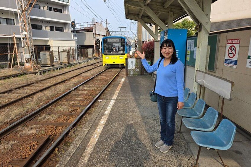 A train station platform with a train, a woman, and blue chairs. 5