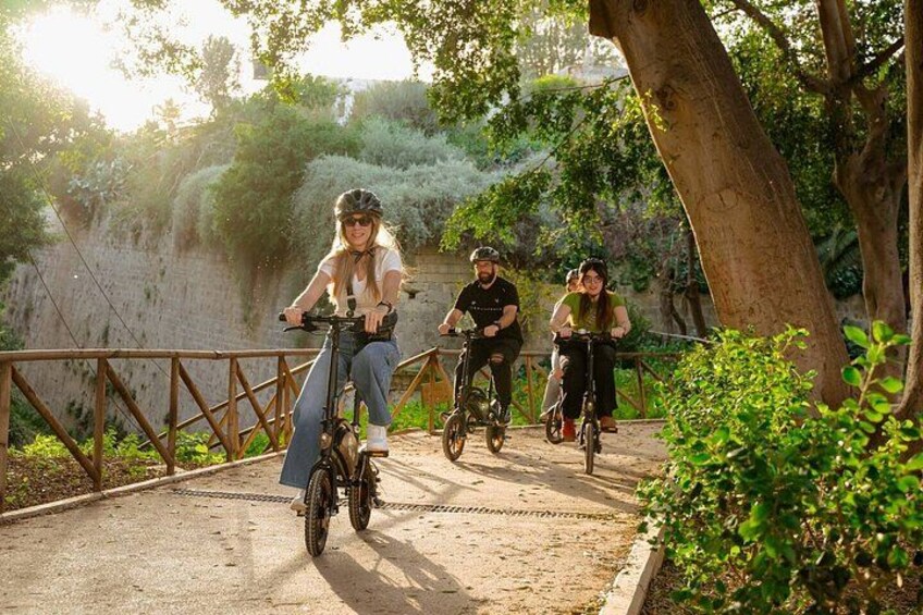Three people riding bicycles on a paved path surrounded by greenery. 4