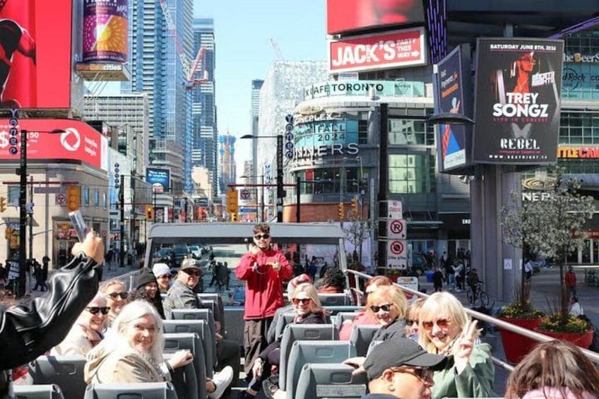 Een levendige stadstraat met mensen in een bus, gebouwen met reclame en een heldere lucht. 5