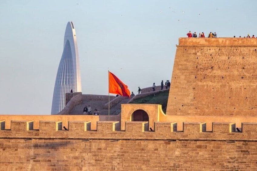 Una fortaleza histórica con un rascacielos moderno al fondo, una bandera en lo alto y personas en los muros. 5