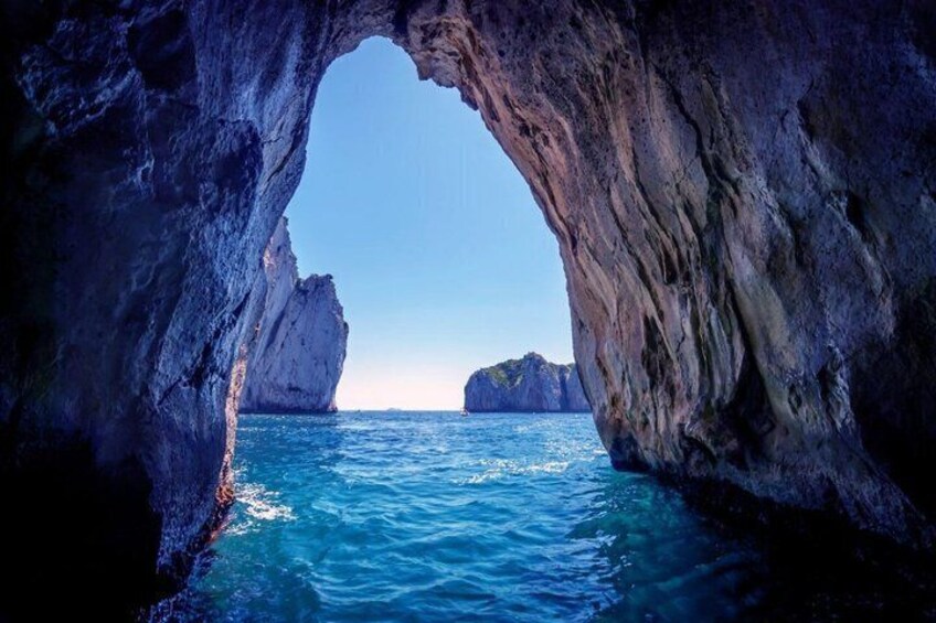 A natural rock arch over a body of water with clear blue water and distant landforms. 3