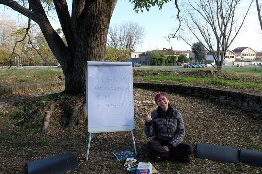 A person sitting next to a whiteboard with handwritten text, a tree, and a park setting. 2