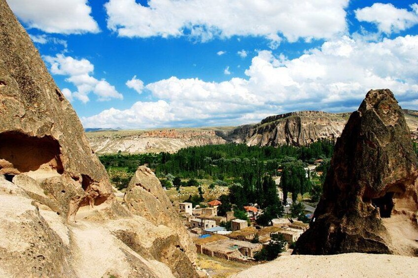 A rugged landscape with prominent rock formations, a village with traditional buildings, and a mountainous backdrop under a partly cloudy sky. 4