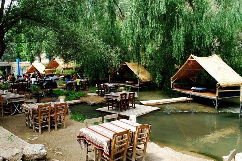 A riverside dining area with tables and chairs, wooden bridges, and thatched-roof huts. 5