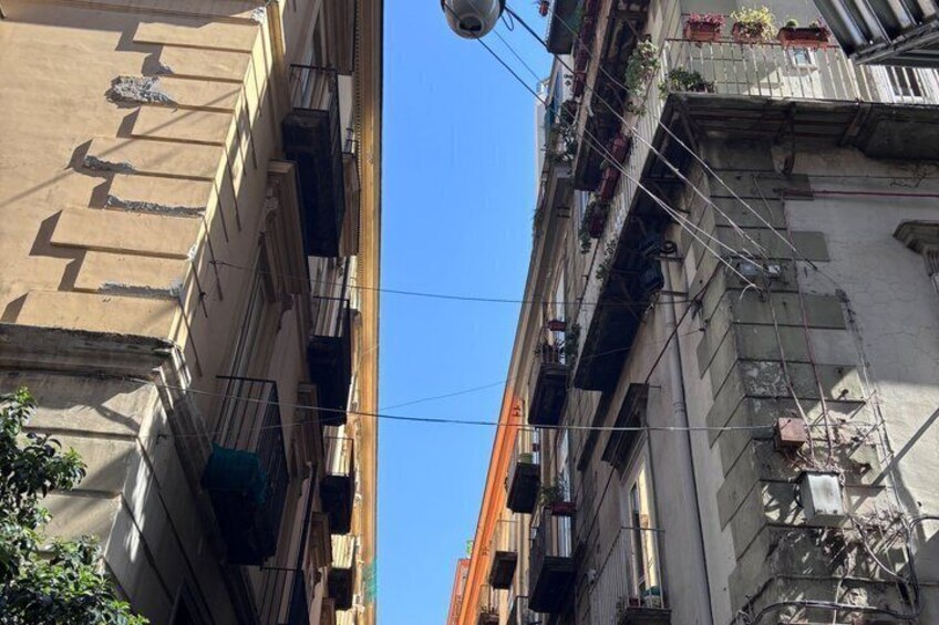 A narrow street between buildings with balconies, some with plants. 4