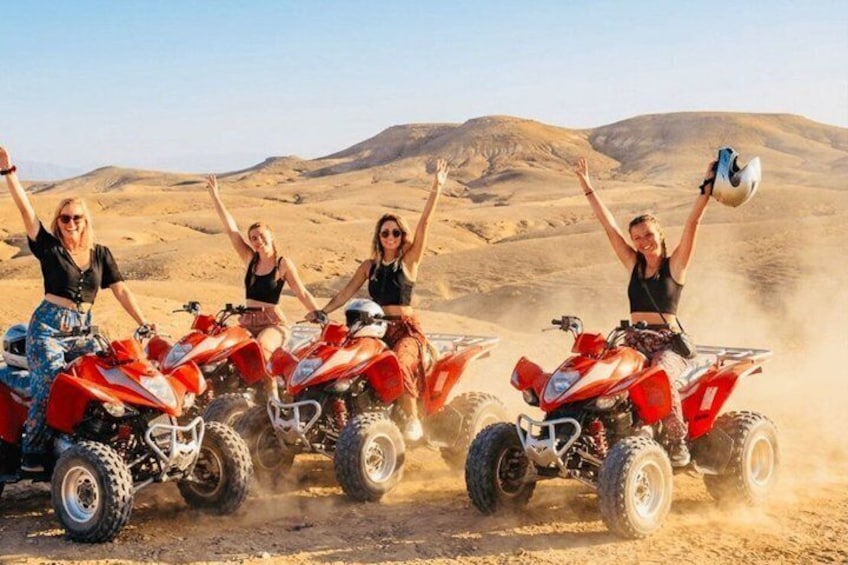 Four people on red ATVs in a desert with sand dunes in the background. 3