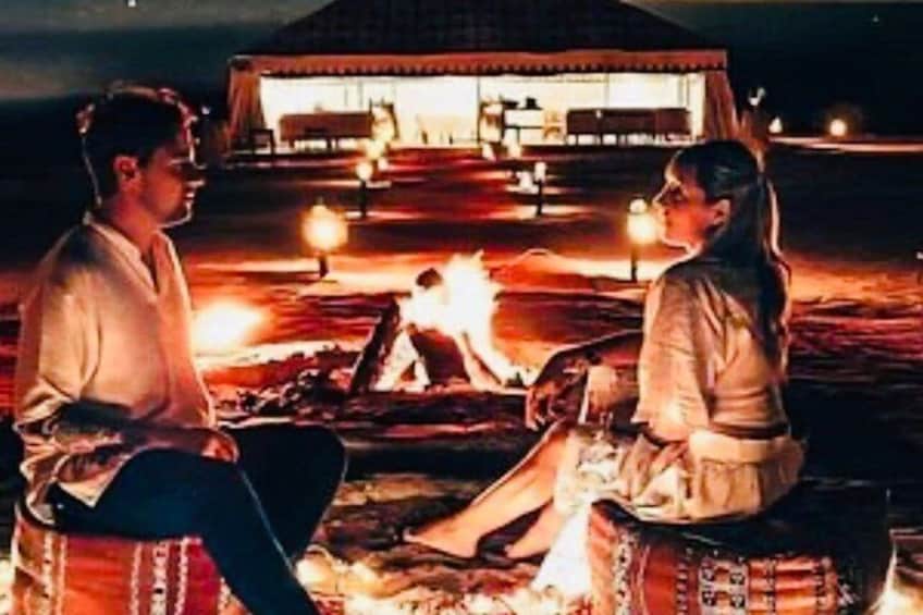 Two people sitting by a campfire at night with a building in the background. 4