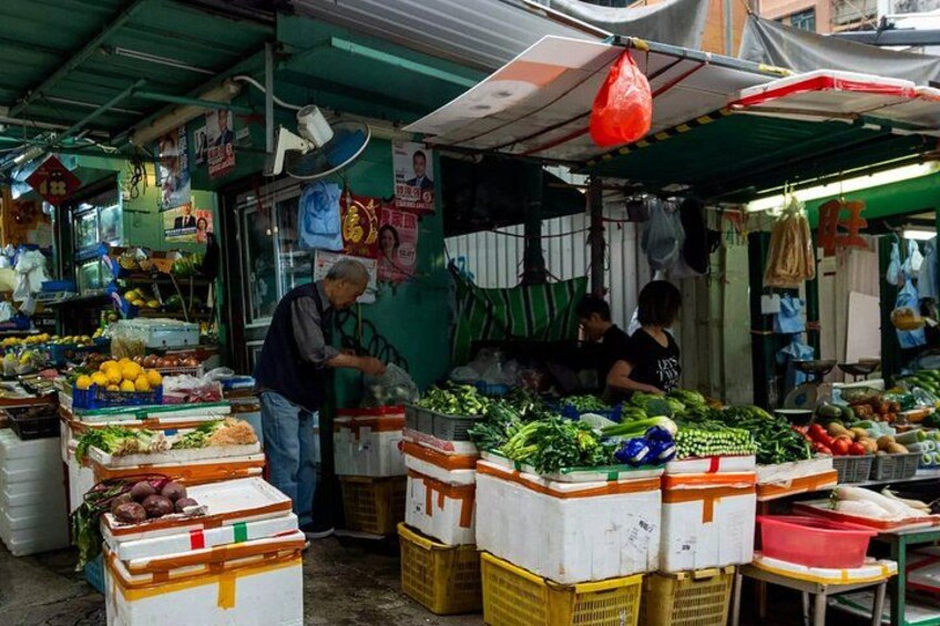 Ein Marktstand mit frischen Lebensmitteln, darunter Obst und Gemüse, sowie eine Person, die Waren bearbeitet. 5