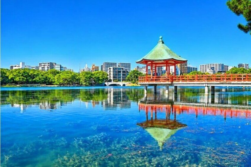 Ein klarer See mit einem Pavillon auf einem Steg, umgeben von Gebäuden und Bäumen. 5