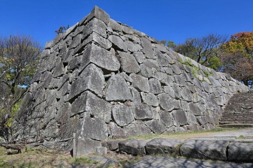 Eine große Steinstruktur mit gestuftem Sockel und flacher Spitze, umgeben von Bäumen und blauem Himmel. 3