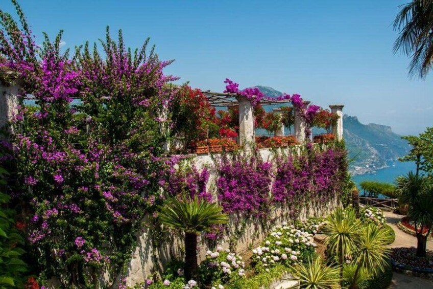 Un giardino costiero con piante fiorite, una struttura in pietra e vista sul mare. 4