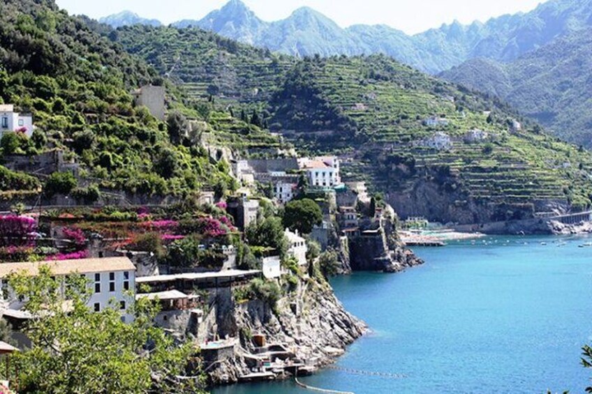 A coastal village with terraced houses, a rocky shoreline, and mountains in the background. 5