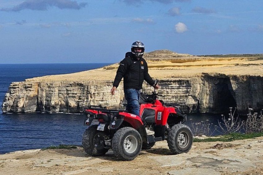 A person on a red ATV near a cliff by the sea. 2