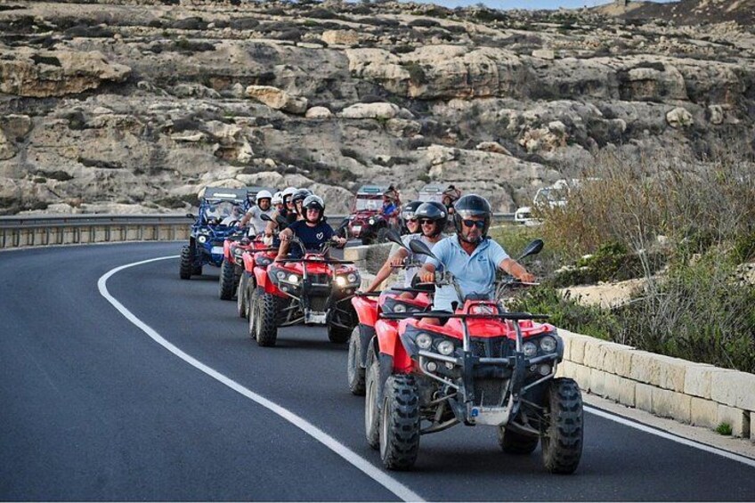 Un grupo de personas conduciendo vehículos todo terreno por un camino sinuoso con terreno rocoso y vegetación escasa al fondo. 3