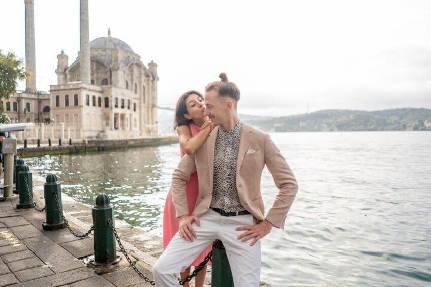 A couple embracing by a waterfront with a historic building in the background. 5