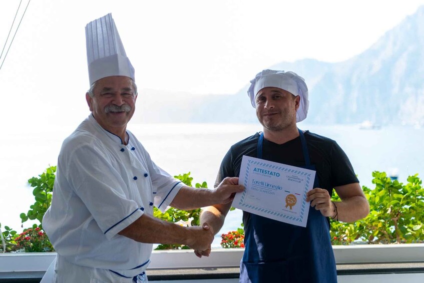 Two individuals shaking hands, one in a chef's uniform and the other in a chef's hat, with a certificate in the background. 2