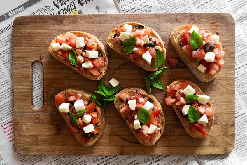 Five pieces of bruschetta on a wooden board, each topped with tomatoes, mozzarella, and basil. 3