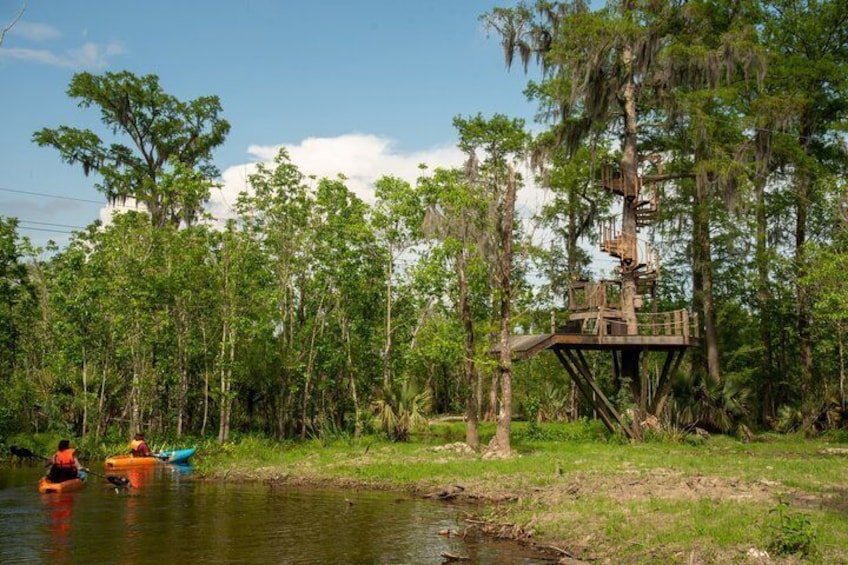 A wooden platform in a forested area by a river with kayaks. 1