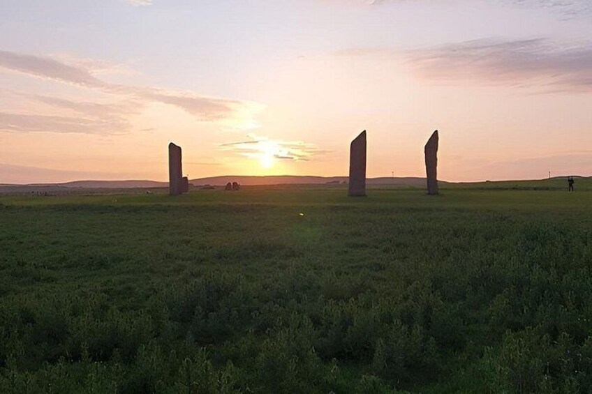 Un atardecer sobre un campo cubierto de hierba con tres piedras verticales. 3