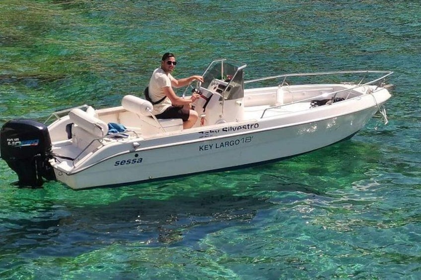Een witte motorboot genaamd 'Key Largo 18' met een persoon aan het roer, op helder turquoise water. 3
