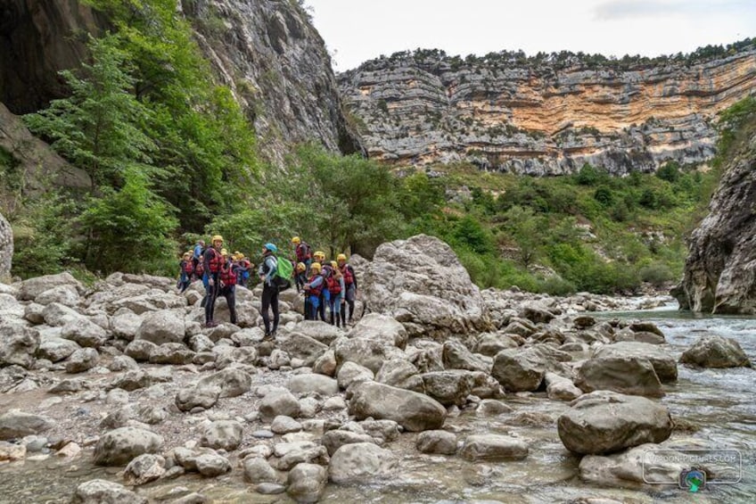Eine Gruppe Wanderer bewegt sich über unwegsames Gelände, im Hintergrund fließt ein Fluss. 5