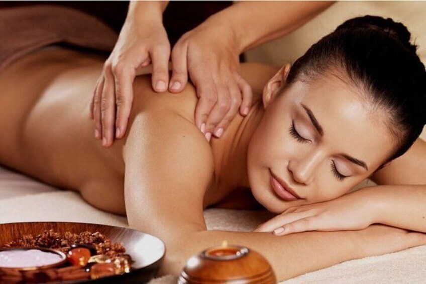 A person receiving a massage with a wooden massage table, a bowl of snacks, and a bottle of oil. 4