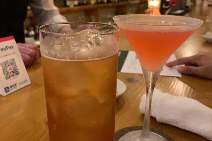 A glass of beer and a pink cocktail on a wooden table with a PayPal QR code. 3
