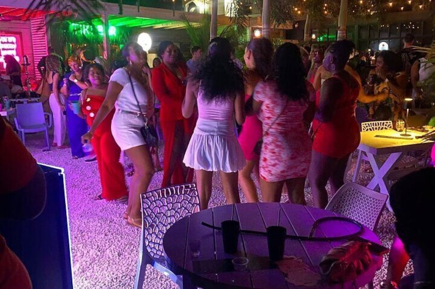 A group of people dancing at an outdoor event with tables and chairs. 1