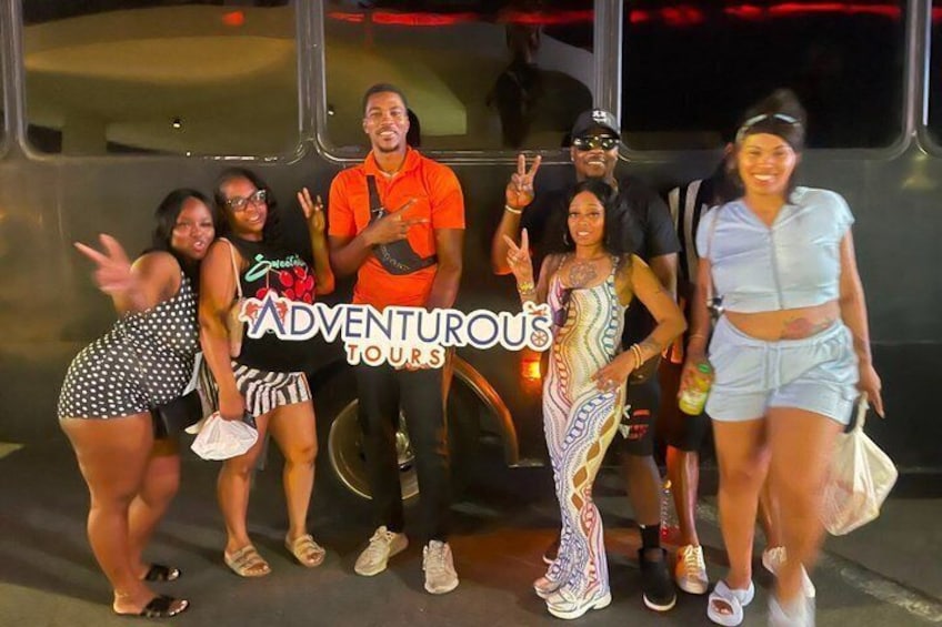 Un grupo de personas posando frente a un autobús con el texto 'ADVENTUROUS TOURS' a la vista. 1