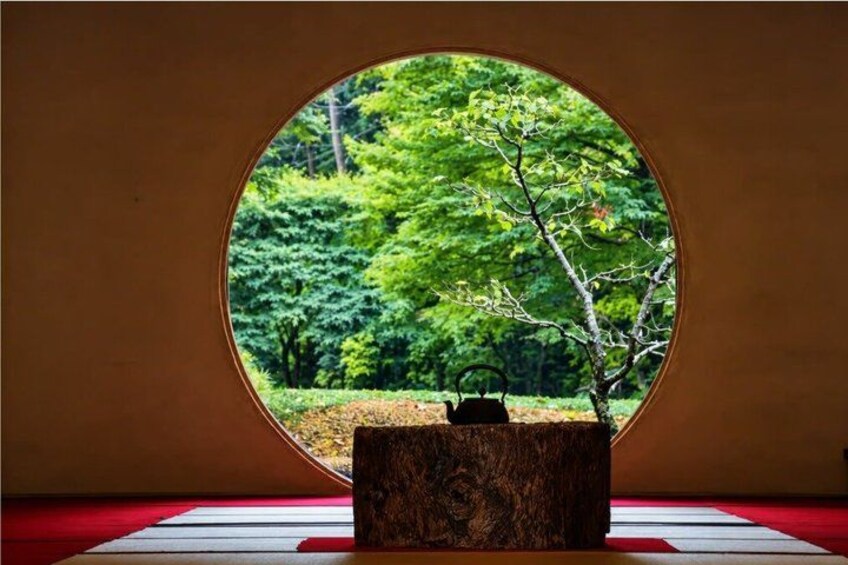 Ein traditioneller japanischer Raum mit Tatami-Böden, einem Holztisch und einem runden Fenster mit Blick auf einen üppigen Garten. 3