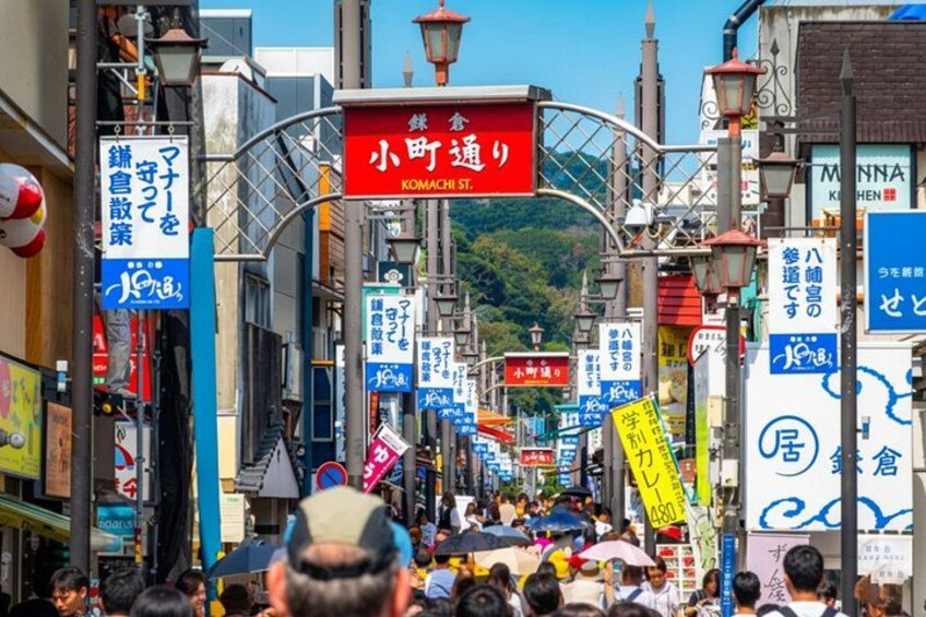 Eine belebte Straße mit Schildern in japanischer Schrift, ein rotes Schild für Komachi Street und traditionelle Architektur. 5