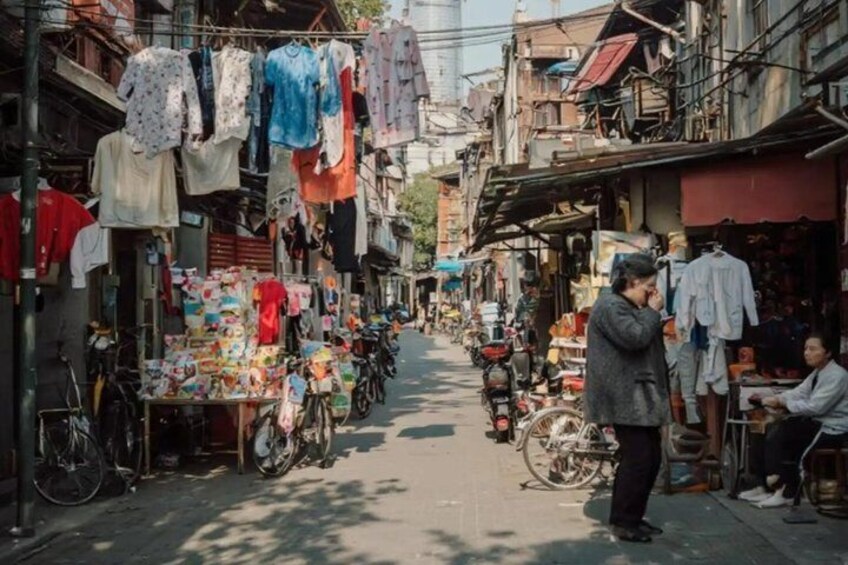 A narrow street with clothing stalls on either side, bicycles parked along the sides, and a person standing in the middle. 4
