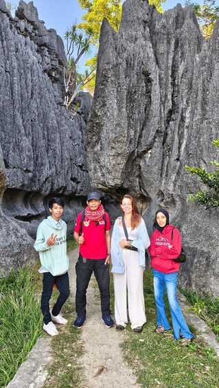 A group of people standing in front of a rocky cliff with trees in the background. 2