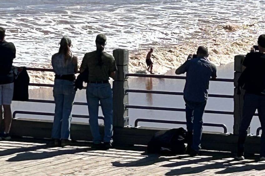 A pier with people standing and watching the ocean. 4