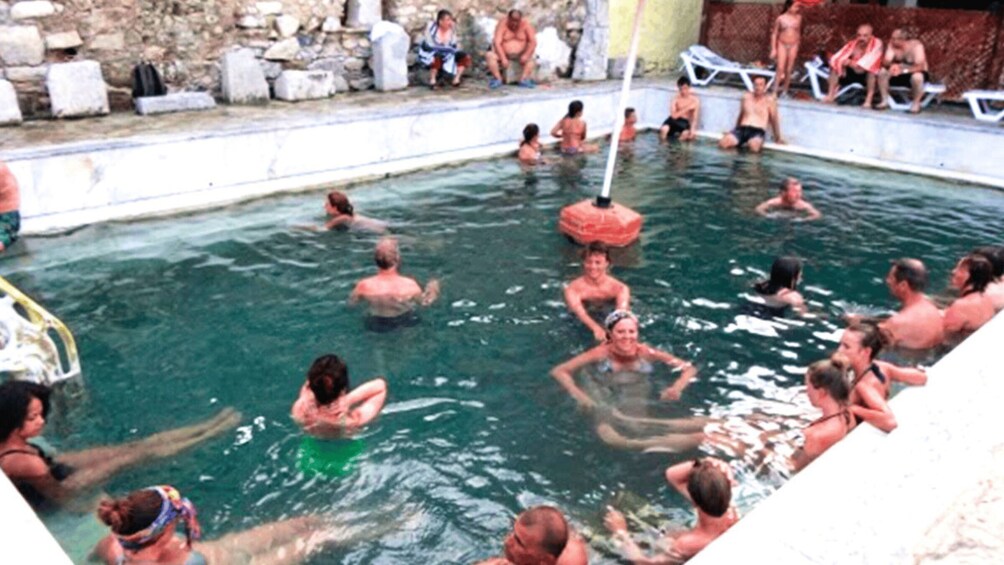 A group of people swimming in a pool with a stone wall in the background. 2