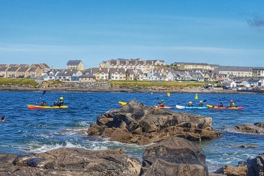 Des personnes pratiquent le kayak sur une côte rocheuse, avec des maisons en arrière-plan. 1