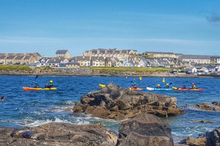 Des personnes pratiquent le kayak sur une côte rocheuse, avec des maisons en arrière-plan. 1