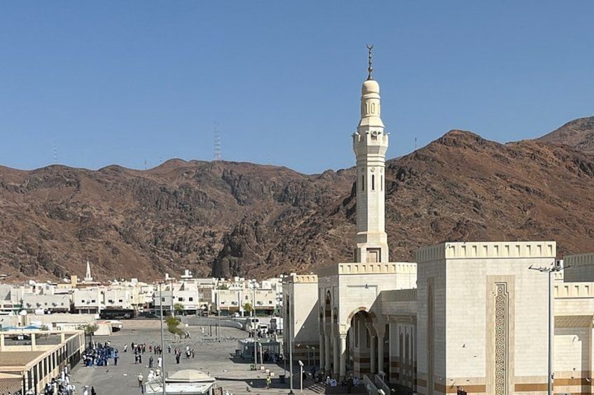 A mosque with a tall minaret, a mosque courtyard, and a mountainous backdrop. 2