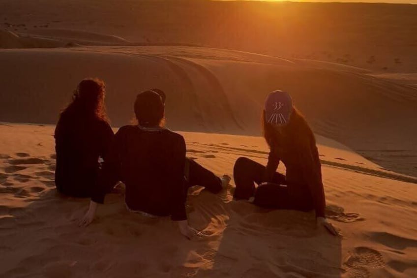 Three people sitting on sand dunes during sunset. 2
