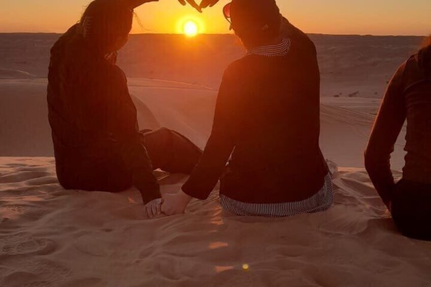 Two people sitting on sand dunes facing the sunset. 3