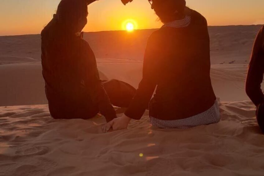 Two people sitting on sand dunes facing the sunset. 4