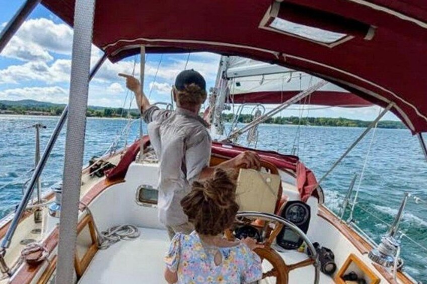 Ein Boot mit einer Person, die in Richtung Horizont deutet, einer Person, die das Steuerrad hält, und einer weiteren Person, die vom Bug aus den Blick in die Ferne richtet. 3